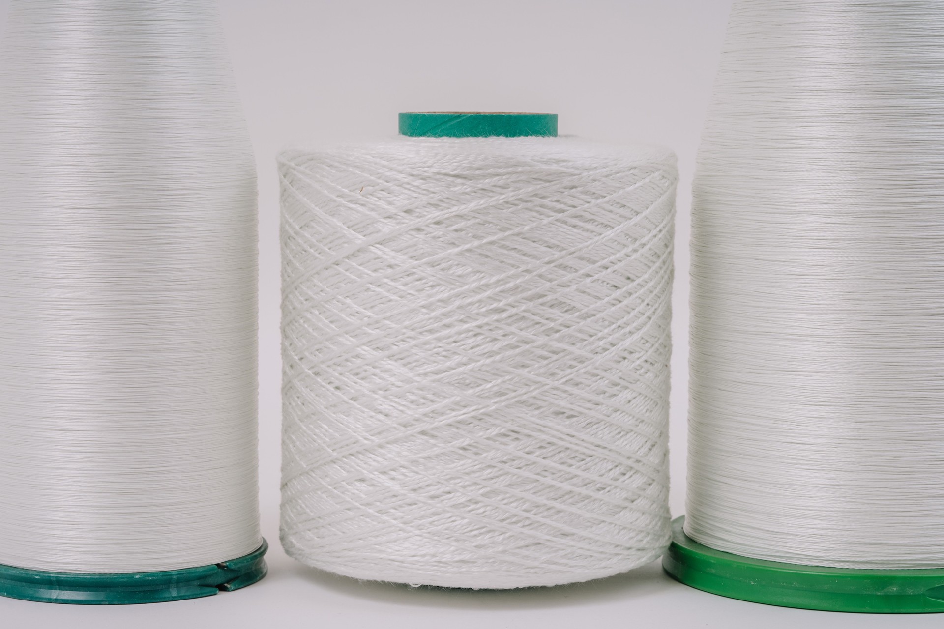 Close-up view of three spools of white fiberglass yarn with different textures, arranged side by side, showcasing their detail and uniformity.